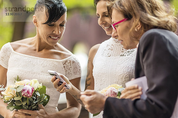 Lesbisches Ehepaar mit Priester beim Blick aufs Handy