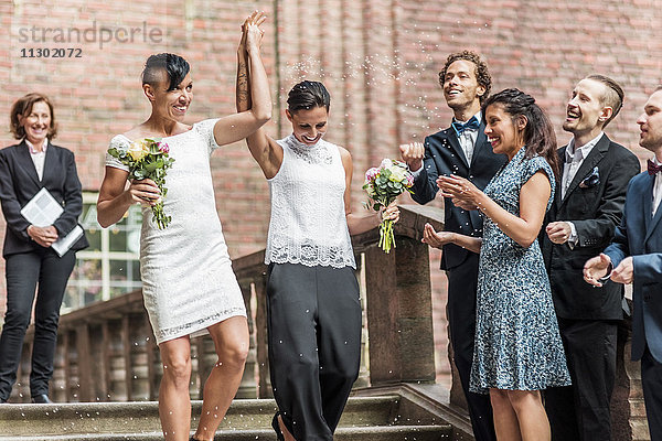 Flachwinkelansicht des fröhlichen lesbischen Paares auf der Treppe mit erhobenen Händen von Freunden