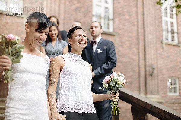 Flachwinkelansicht des glücklichen lesbischen Paares auf der Treppe mit Gästen im Hintergrund