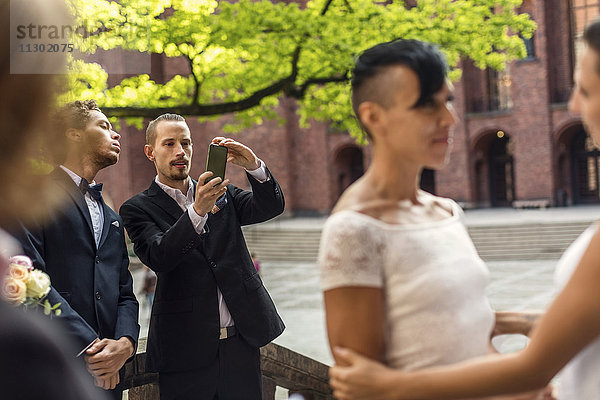 Mann fotografiert lesbisches Paar während der Hochzeitszeremonie