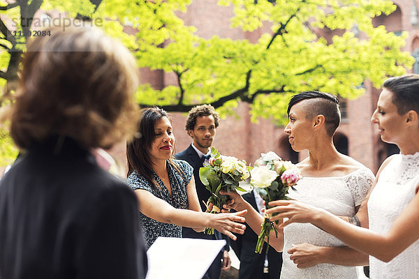 Lesbisches Ehepaar überreicht Blumensträuße an Gäste während der Hochzeitszeremonie