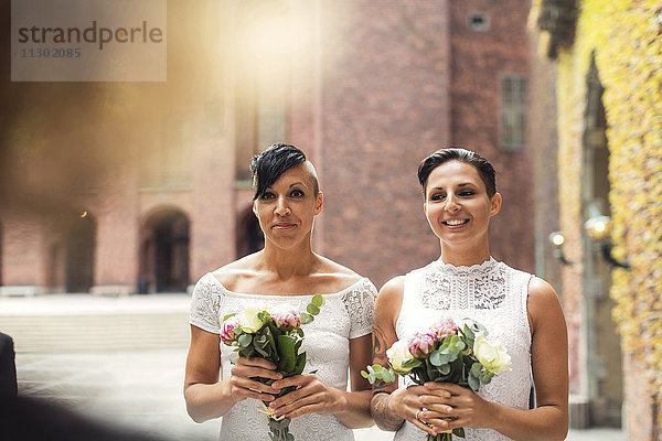 Glückliches lesbisches Paar mit Blumensträußen während der Hochzeitszeremonie