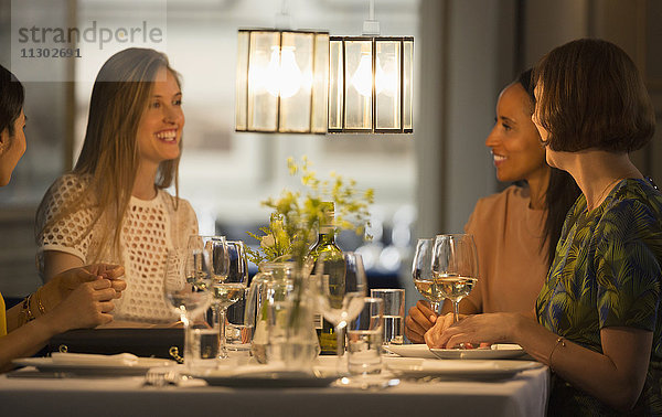 Lächelnde Freundinnen beim Essen und Trinken von Wein am Restauranttisch