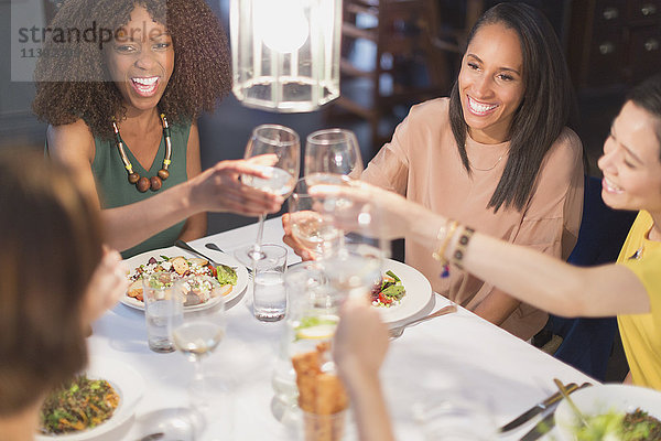 Lächelnde Freundinnen trinken Weißweingläser am Restauranttisch