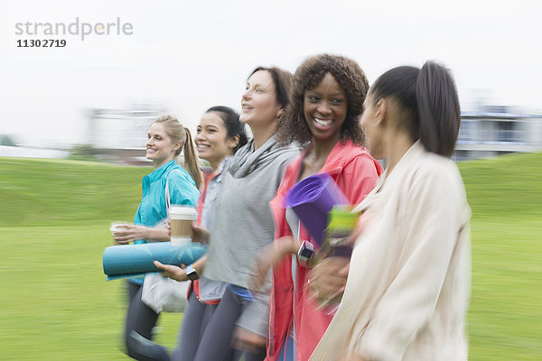 Lächelnde Frauen  die mit Yogamatten und Kaffee spazieren gehen.