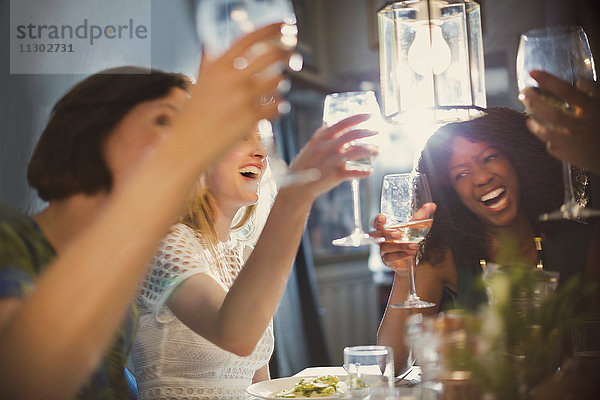 Lachende Freundinnen stoßen im Restaurant auf Weißweingläser an.
