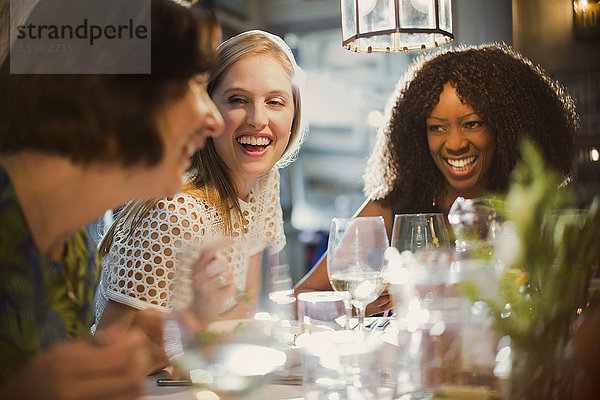 Lachende Frauenfreunde beim Reden und Essen am Restauranttisch