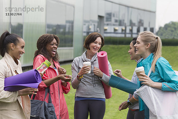 Freundinnen mit Yogamatten und Kaffee außerhalb des Fitnessstudios