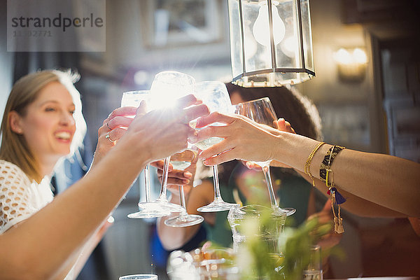 Lächelnde Frauenfreunde stoßen auf Weingläser an  die am Restauranttisch speisen.