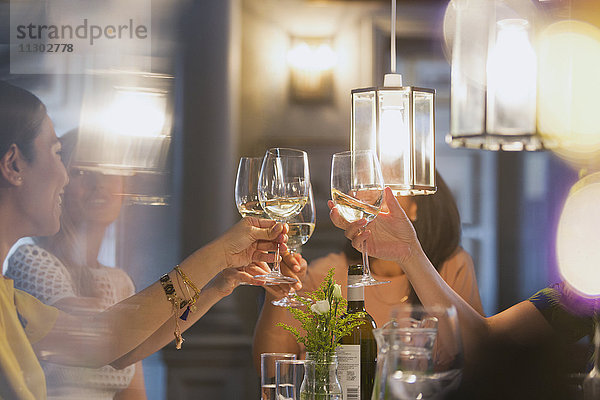 Weibliche Freunde stoßen auf Weißweingläser an  die am Restauranttisch speisen.