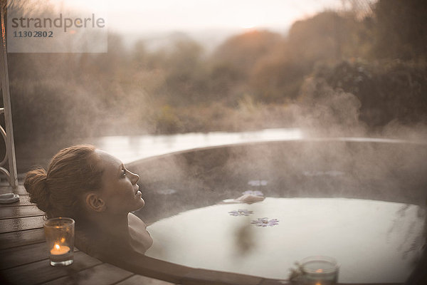 Gelassene Frau im dampfenden Whirlpool mit Blick auf herbstliche Bäume