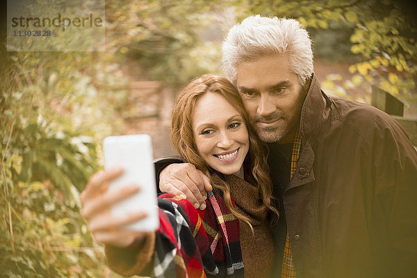 Paar  das sich umarmt und ein Selfie mit einem Fotohandy im Garten macht