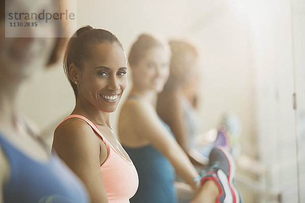 Portrait lächelnde Frauen  die ihre Beine an der Stange im Fitnessstudio ausstrecken.
