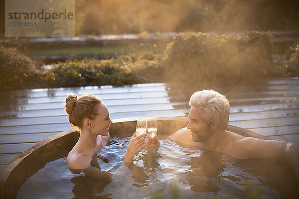 Paar stößt mit Sektgläsern im Whirlpool auf der Herbstterrasse an