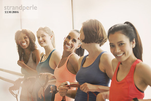 Lächelnde Frauen halten Widerstandsbänder an der Stange im Fitnessstudio der Übungsklasse