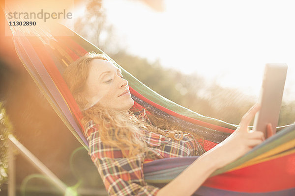 Frau entspannt sich in sonniger Hängematte mit digitalem Tablet