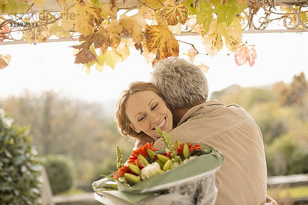 Ehemann überrascht Frau mit Blumenstrauß auf Herbstterrasse