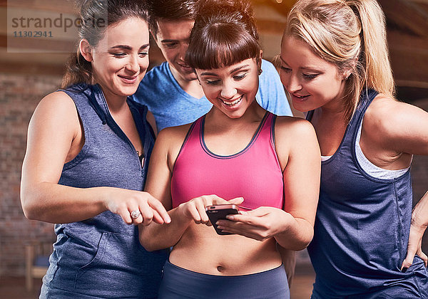 Junge Frauen und Männer in Sportbekleidung SMS mit Handy