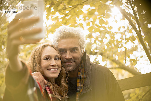 Lächelndes Paar nimmt Selfie mit Kamera-Handy unter Herbstbaum