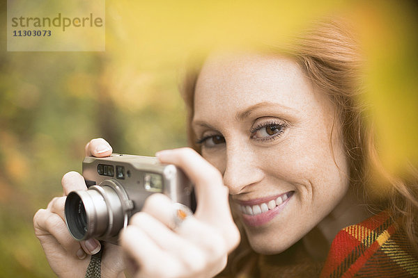 Nahaufnahme einer lächelnden Frau mit Digitalkamera inmitten von Herbstblättern