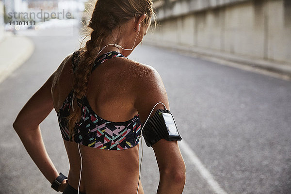 Fitte Läuferin im Sport-BH mit mp3-Player-Armband und Kopfhörern  die sich auf einer städtischen Straße ausruht