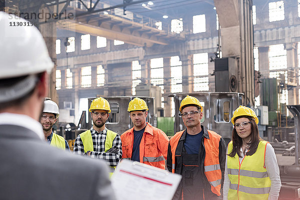 Stahlarbeiter hören dem Manager beim Treffen in der Fabrik zu