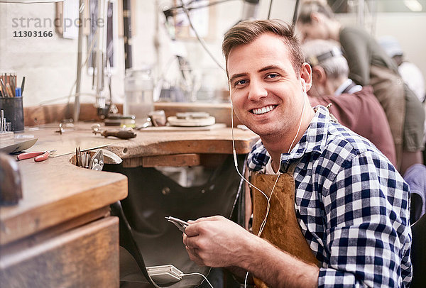 Portrait lächelnder Juwelier beim Musikhören mit Kopfhörern in der Werkstatt
