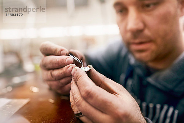 Fokussierter männlicher Juwelier  der Schmuck in der Werkstatt zusammenbaut.