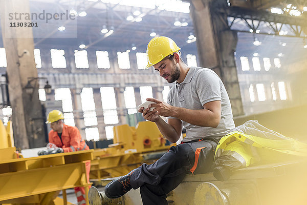 Stahlarbeiter texten mit Handy bei einer Pause in der Fabrik