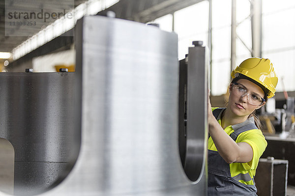 Stahlbauerin untersucht Stahlteil in der Fabrik