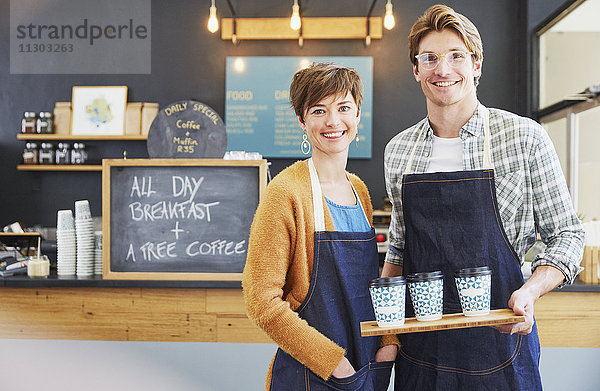 Porträt selbstbewusster Cafébesitzer in Jeansschürzen  der ein Tablett mit Kaffeetassen hält