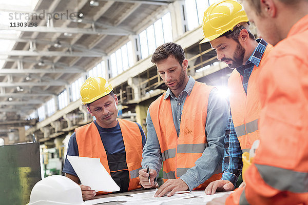 Stahlarbeiter und Ingenieure treffen sich zur Begutachtung von Bauplänen in der Fabrik