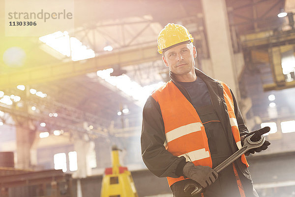 Porträt eines selbstbewussten Stahlarbeiters mit großem Schraubenschlüssel in der Fabrik