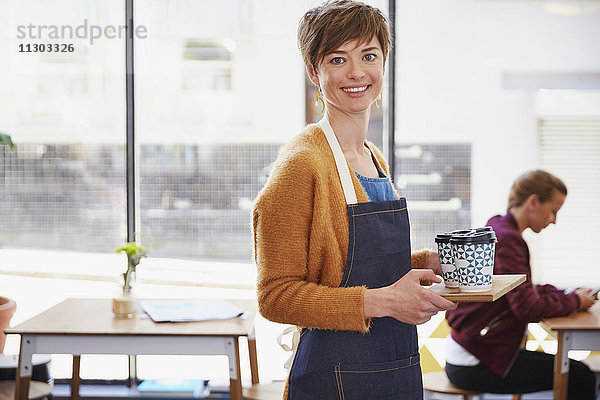 Porträt einer selbstbewussten Café-Besitzerin  die in einem Café Kaffee auf einem Tablett serviert