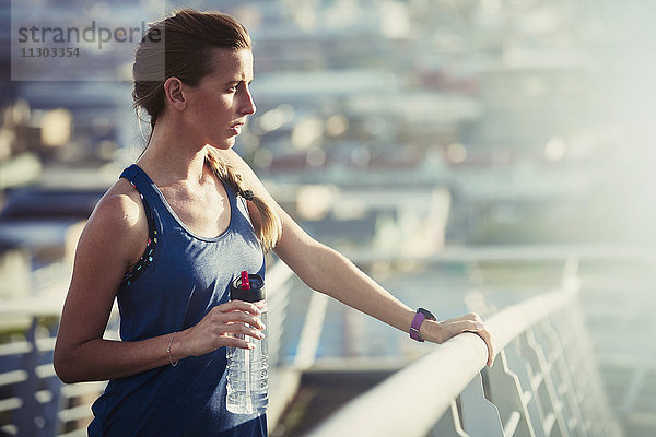Läuferin mit Wasserflasche  die sich auf einer sonnigen Fußgängerbrücke ausruht