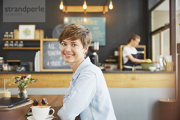 Porträt einer lächelnden Frau  die am Kaffeetisch Kaffee trinkt