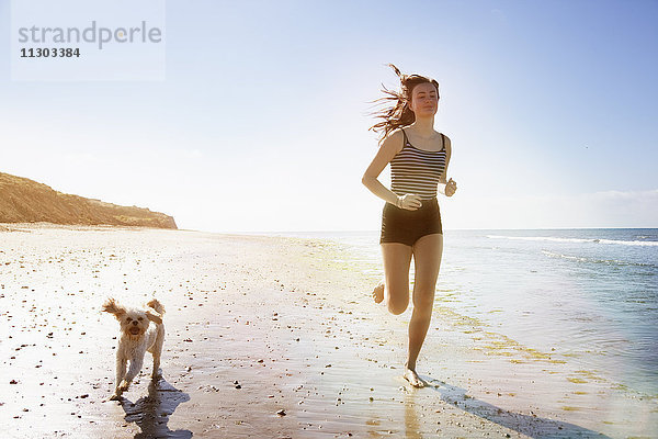 Junge Frau und Hund beim Laufen am sonnigen Strand