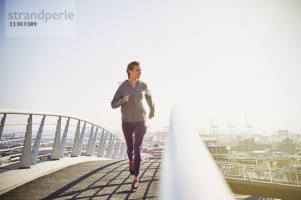 Weibliche Läuferin läuft auf einer sonnigen Fußgängerbrücke bei Sonnenaufgang