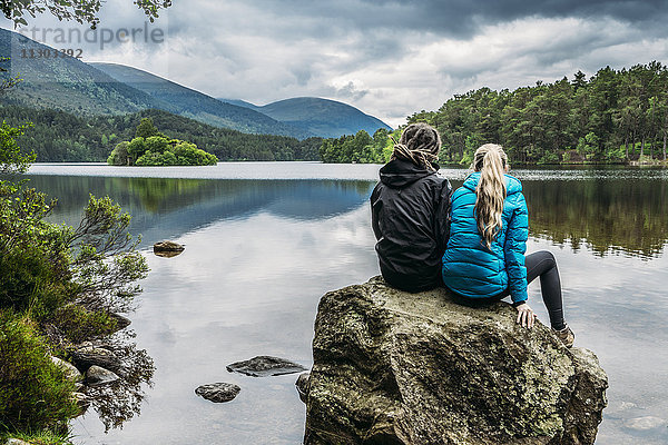 Paar auf Felsen sitzend mit Blick auf den ruhigen See  Loch an Eilein  Schottland