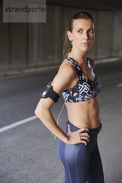 Serious fit Läuferin in Sport-BH mit mp3-Player-Armband und Kopfhörer auf städtischen Straße