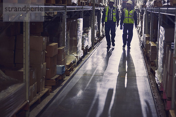 Arbeiter gehen entlang der Waren in den Regalen im Gang eines Vertriebslagers