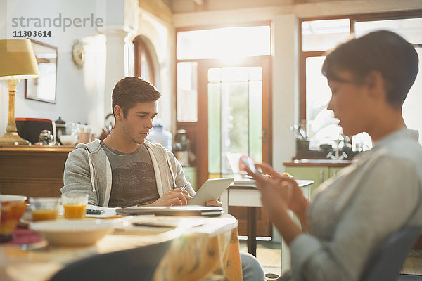 Junges Studentenpaar mit Handy und digitalem Tablet am Küchentisch