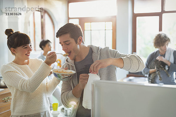 Junge Frau füttert ihren Freund mit Müsli in der Wohnküche