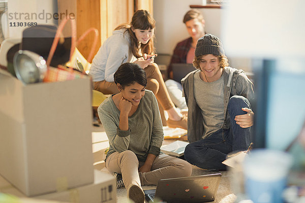 Junge Paare  die einen Laptop benutzen  um Umzugskartons in einer neuen Wohnung auszupacken