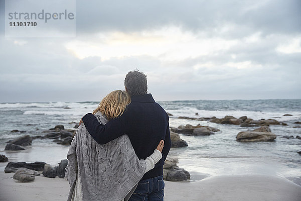 Gelassenes  zärtliches Paar  das sich am Winterstrand umarmt und auf das Meer schaut