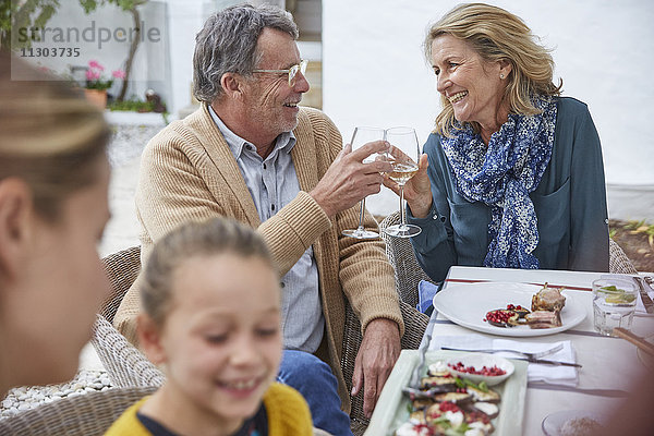 Glückliches älteres Paar stößt beim Mittagessen im Innenhof mit Weißweingläsern an