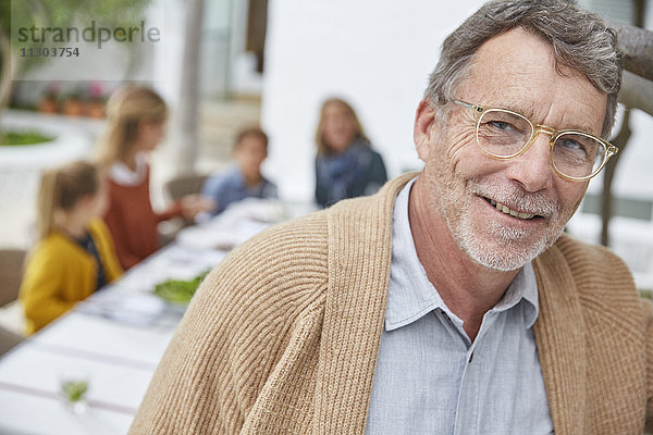 Porträt eines lächelnden älteren Mannes  der mit seiner Familie auf der Terrasse zu Mittag isst