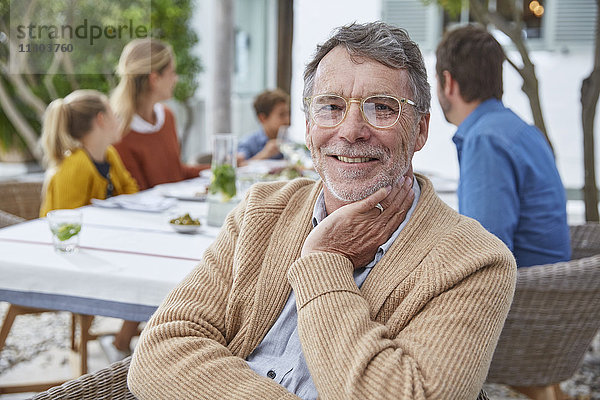 Porträt eines lächelnden älteren Mannes  der mit seiner Familie auf der Terrasse zu Mittag isst