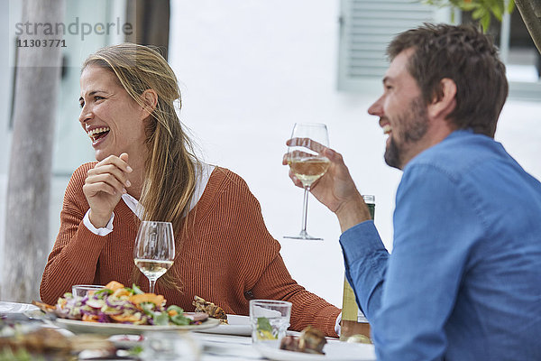 Lachendes Paar trinkt Weißwein und isst zu Mittag am Terrassentisch