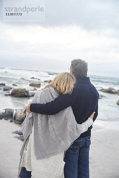 Gelassenes  zärtliches Paar  das sich am Winterstrand umarmt und auf das Meer schaut
